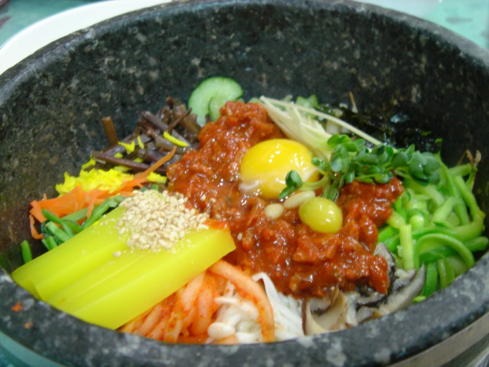 Bibimbap in a hot stone pot topped with yellow mung bean jelly, raw beef and an egg yolk