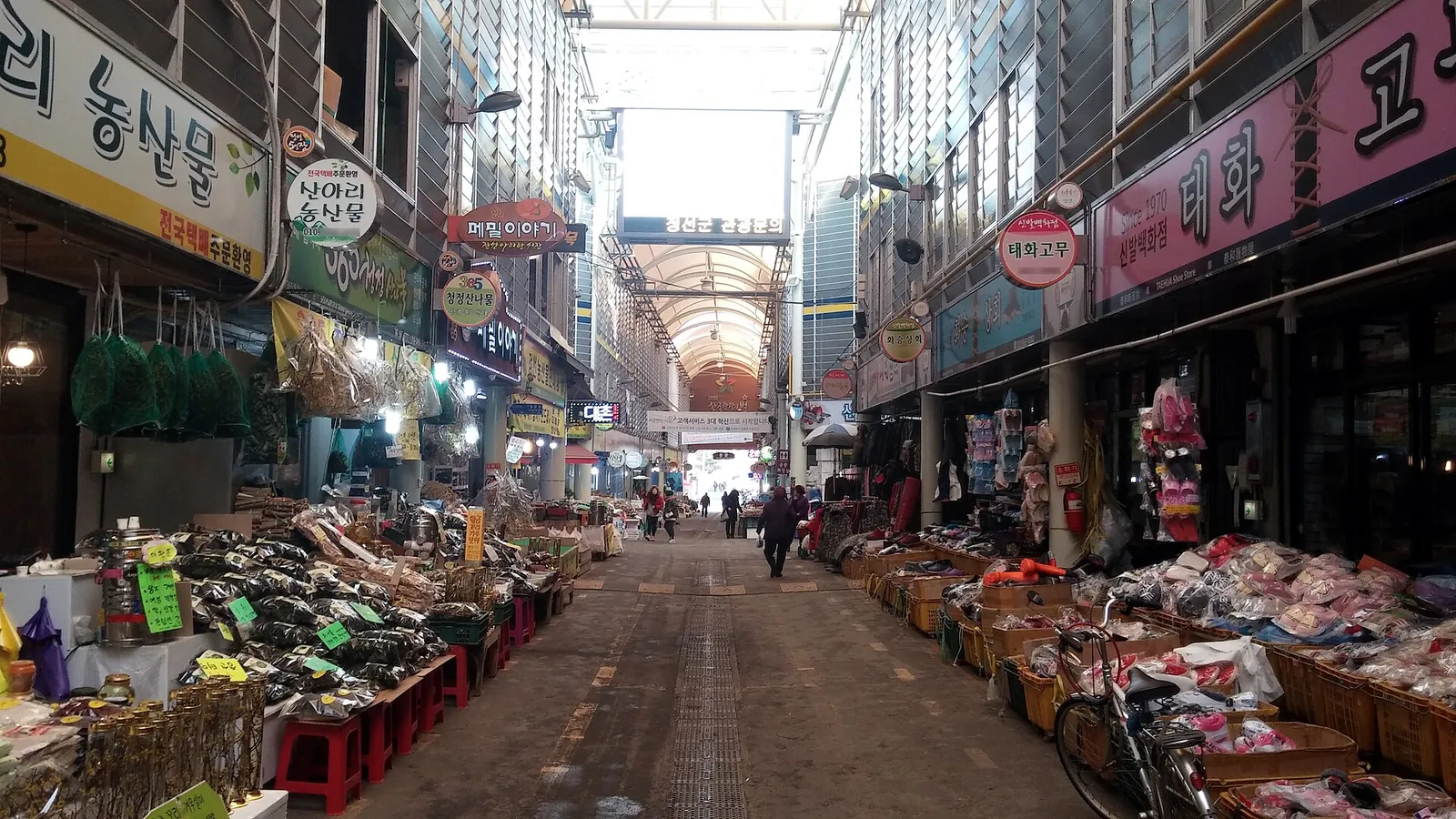 A covered lane of the Jeongseon Arirang Market lined with shops and stalls selling dried herbs, vegetables and goods