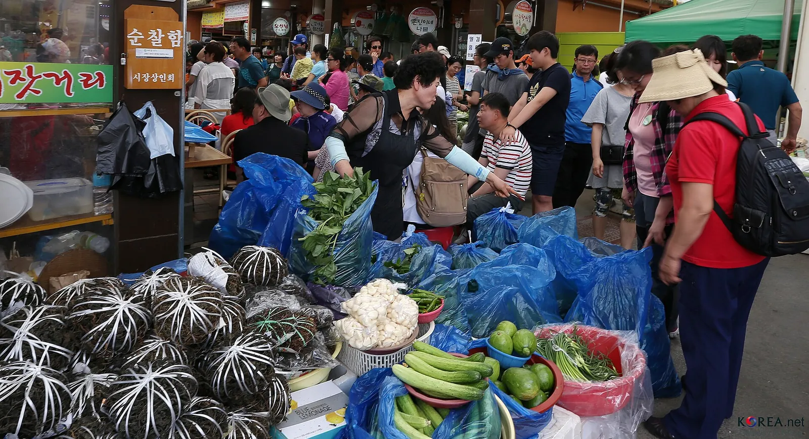 Shoppers browsing bundles of vegetables and produce at a busy stall on market day in Jeongseon