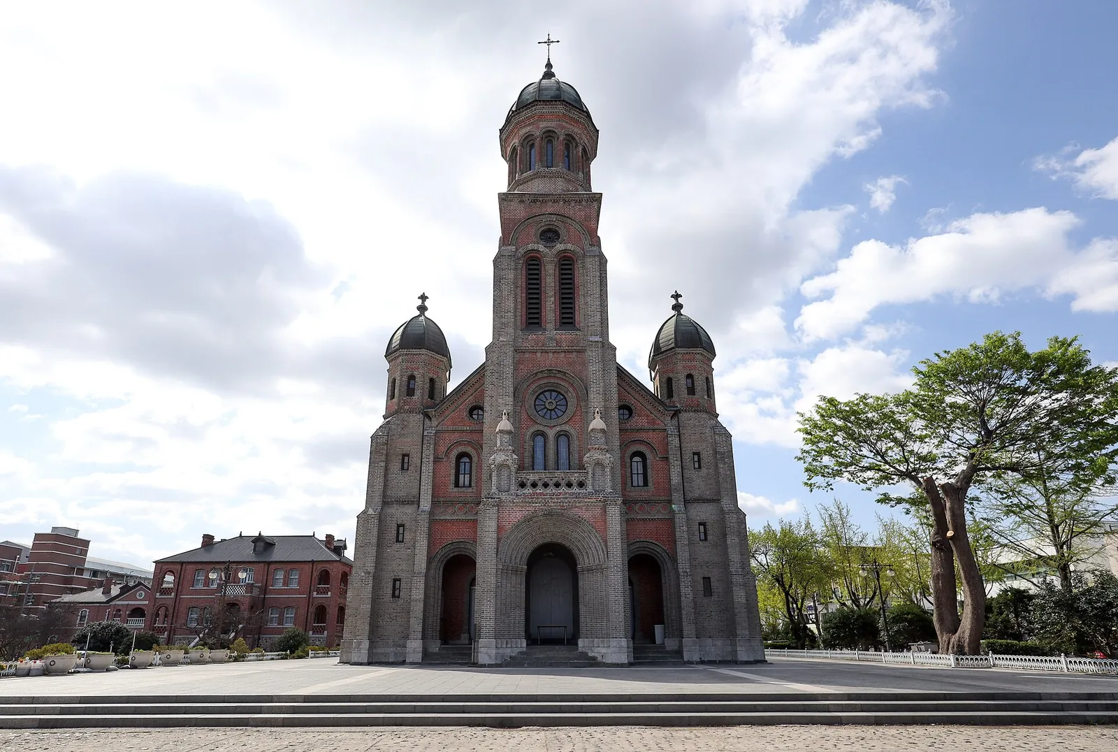 Red-brick front of Jeondong Catholic Cathedral with three domed towers under a blue sky