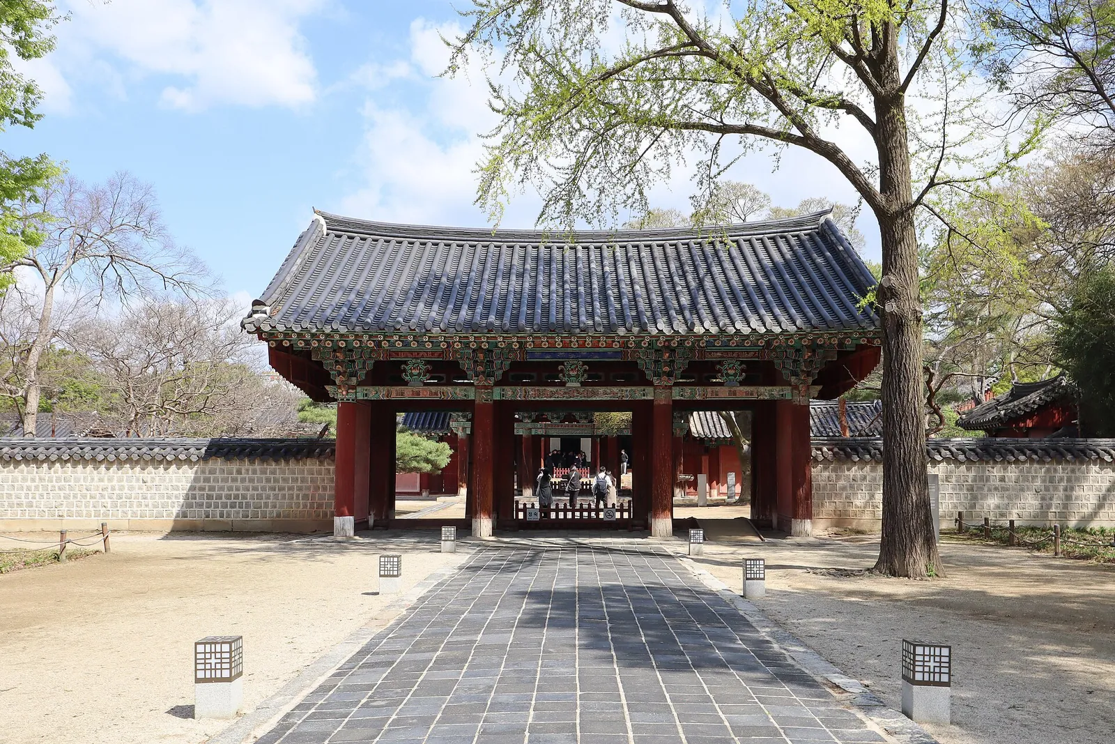 Red-pillared gate of Gyeonggijeon Shrine at the end of a stone path between walls