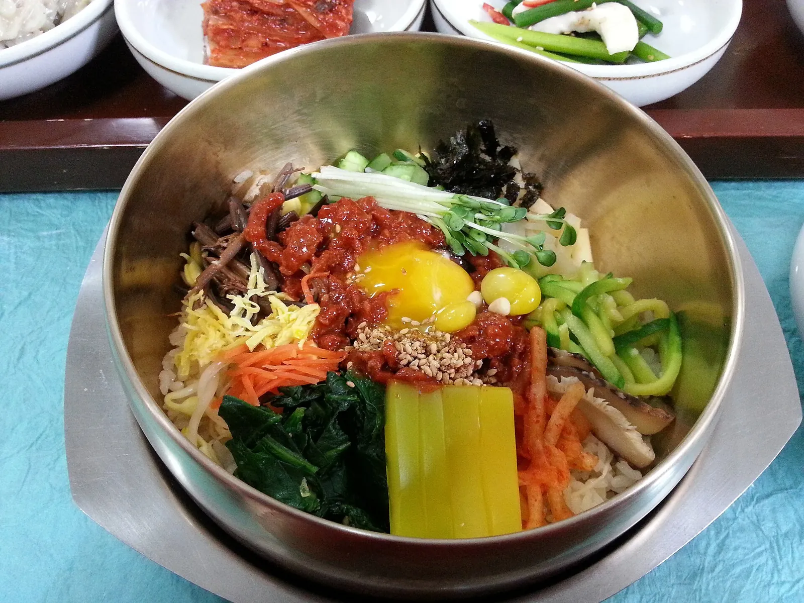 Bibimbap in a brass bowl topped with seasoned vegetables, beef, an egg yolk and yellow mung bean jelly