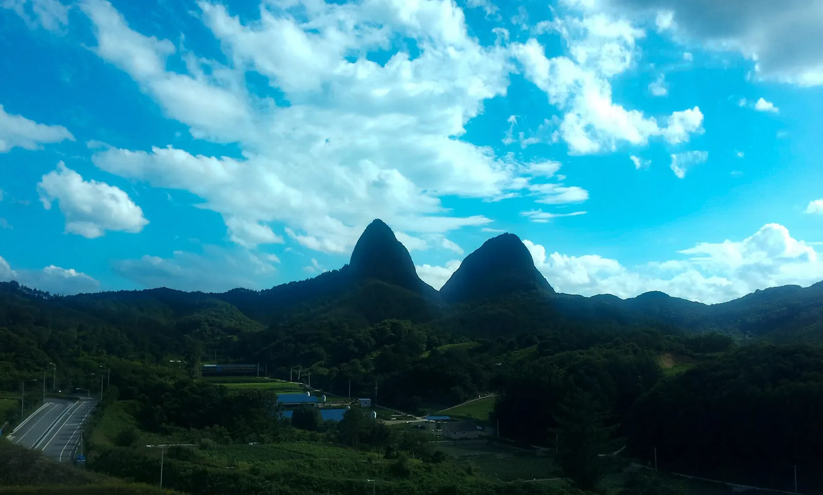 The twin rock peaks of Maisan rising above forested hills under a bright blue sky