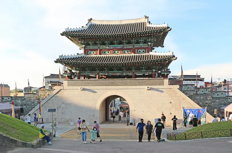 Two-storey Gongbukmun Gate of Jinjuseong Fortress under a blue sky, with visitors on the steps in front
