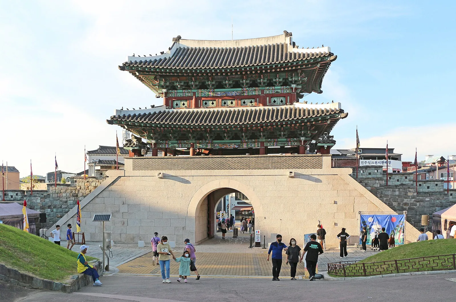 Two-storey Gongbukmun Gate of Jinjuseong Fortress under a blue sky, with visitors on the steps in front
