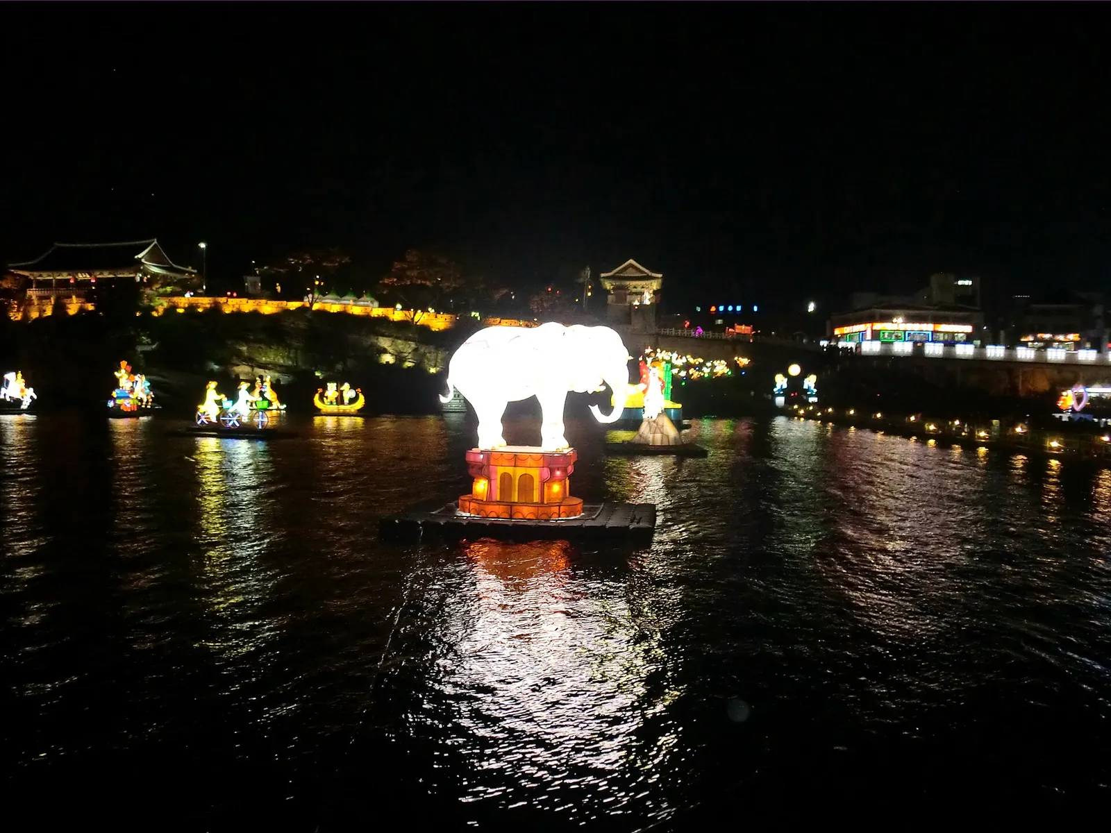 Floating lanterns, including a white elephant figure, lit up on the Namgang River at night during the Jinju Namgang Yudeung Festival
