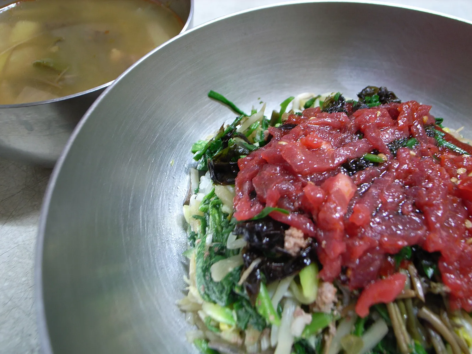 Bowl of Jinju bibimbap topped with seasoned raw beef over vegetables, with soup on the side
