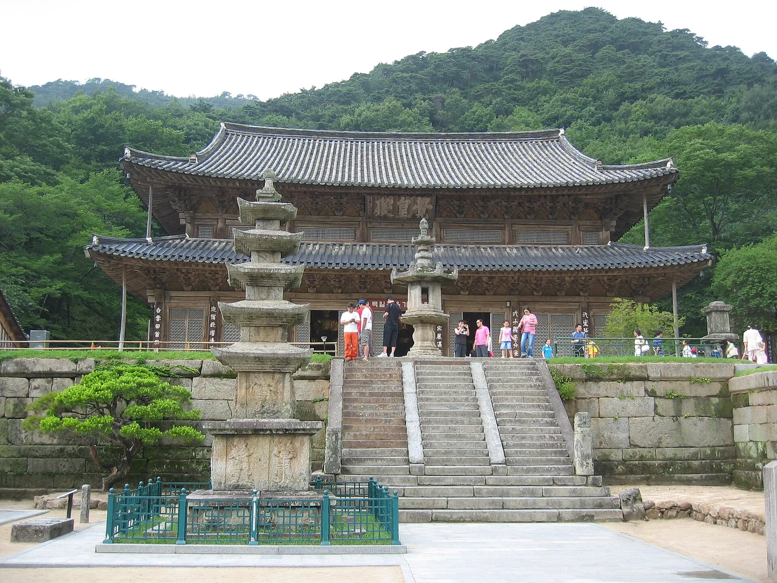 Main hall of Hwaeomsa temple in Gurye with a stone pagoda and lantern on terraces below a forested slope