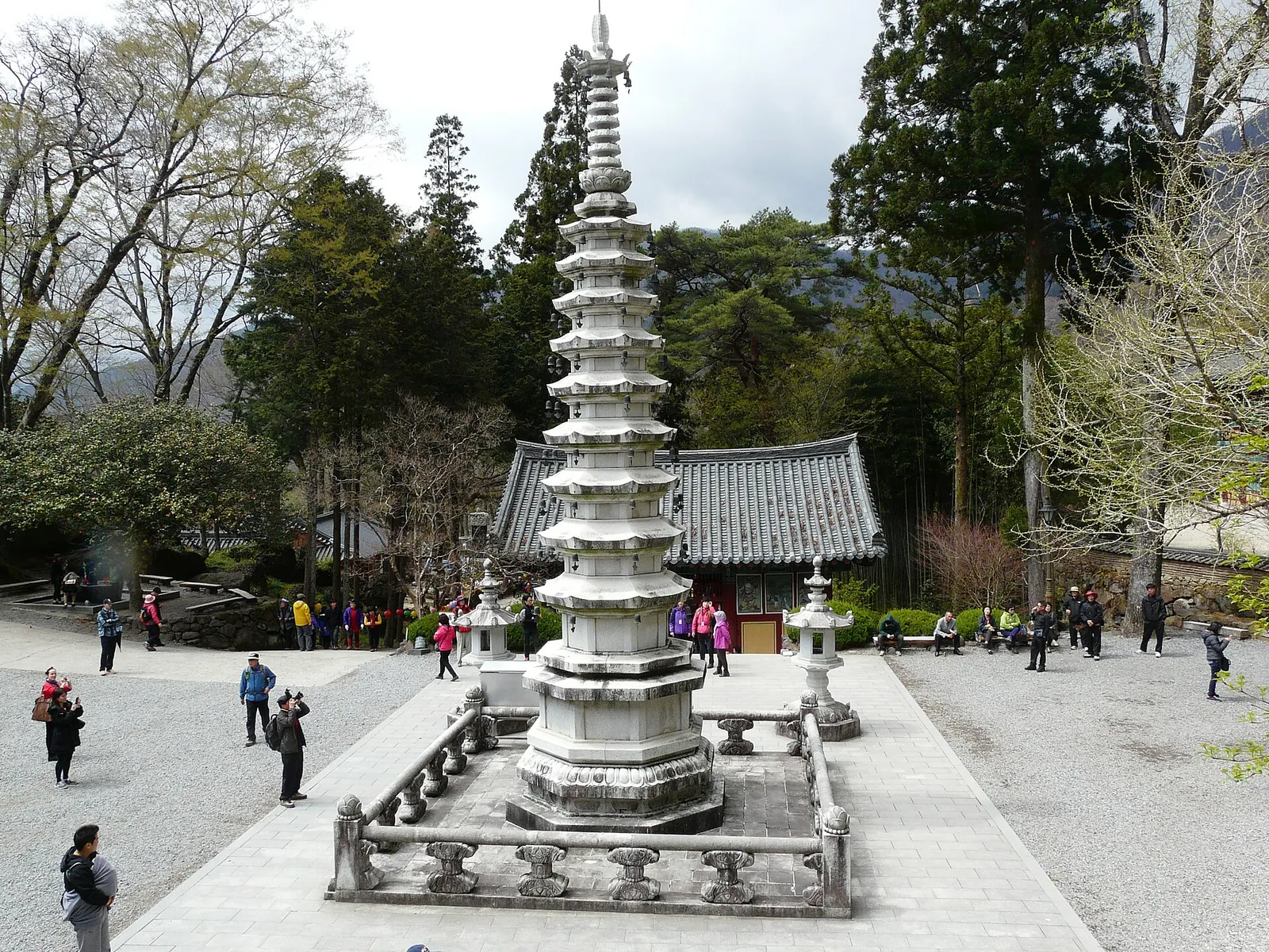 Tall white stone pagoda in the courtyard of Ssanggyesa temple with visitors and trees behind