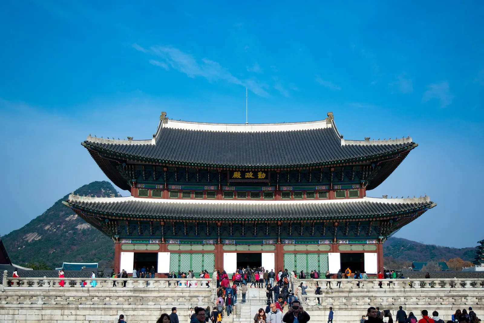 Geunjeongjeon throne hall at Gyeongbokgung Palace with mountains behind and visitors in the courtyard