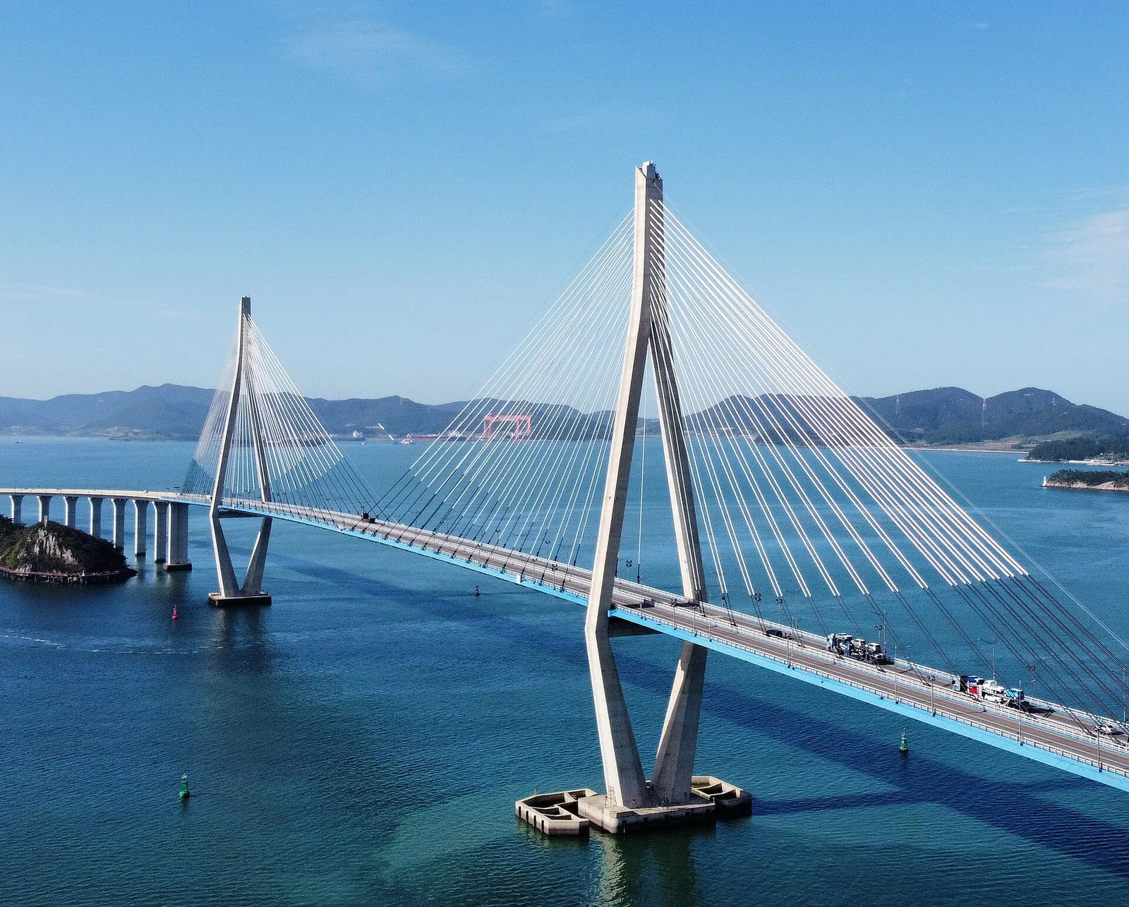White cable-stayed Mokpo Bridge crossing blue water between wooded islands on a clear day