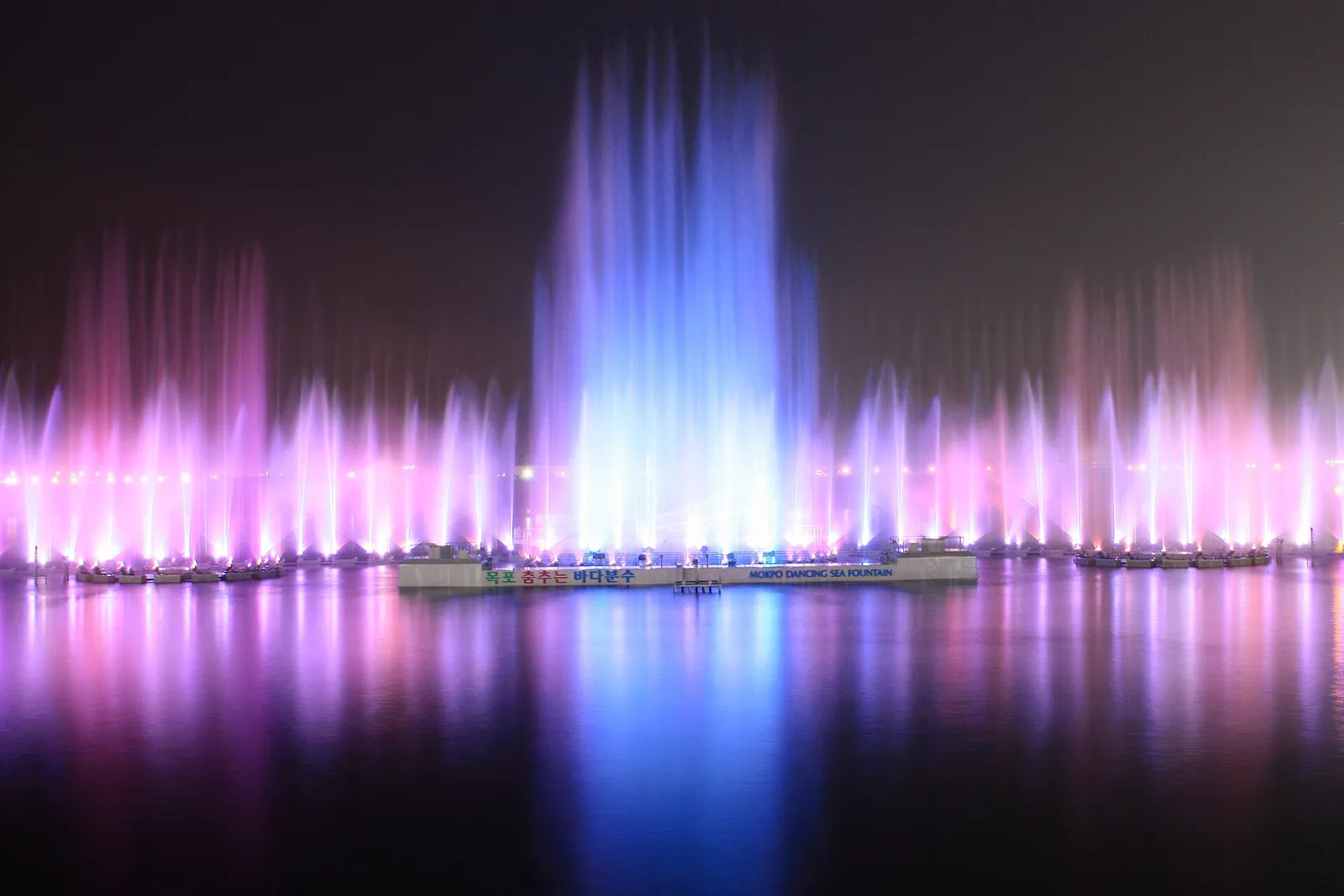 Coloured jets of the musical fountain lit pink and blue against the night sea at Mokpo