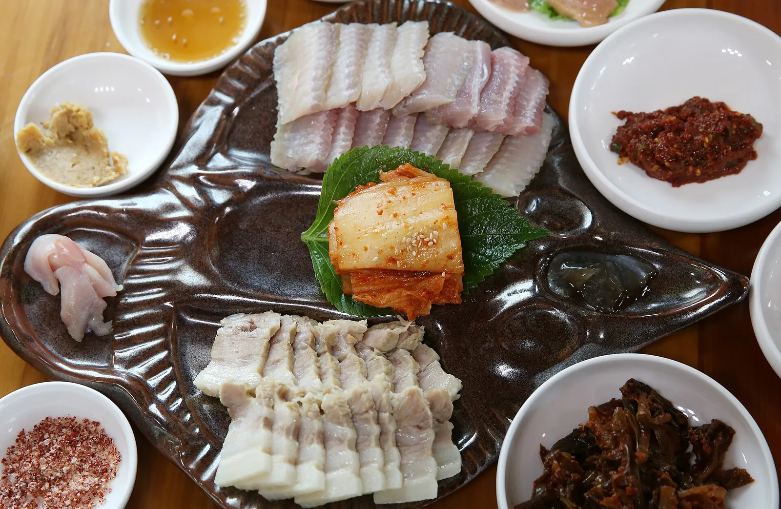 A platter of fermented skate slices with boiled pork and kimchi, surrounded by side dishes