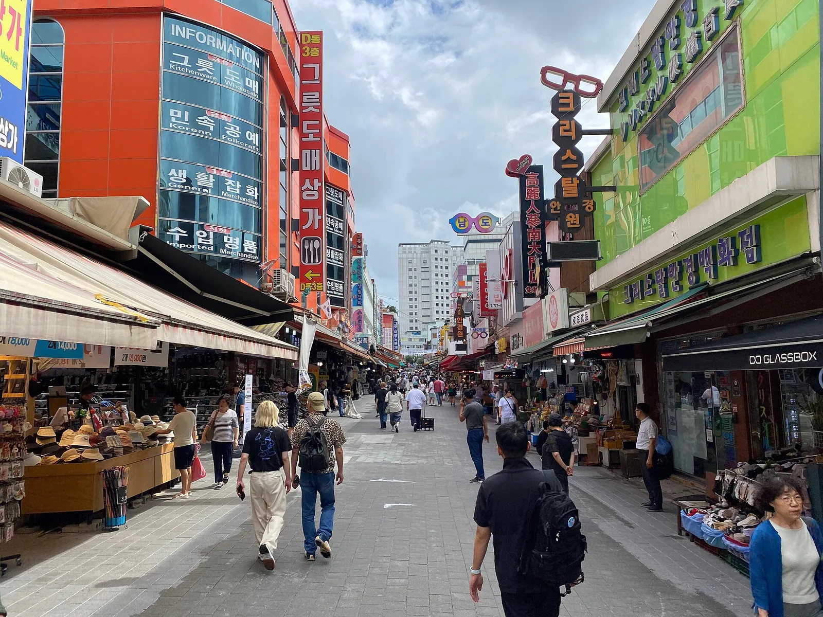 Shoppers on a street lined with shop awnings and signboards in Namdaemun Market on a cloudy day