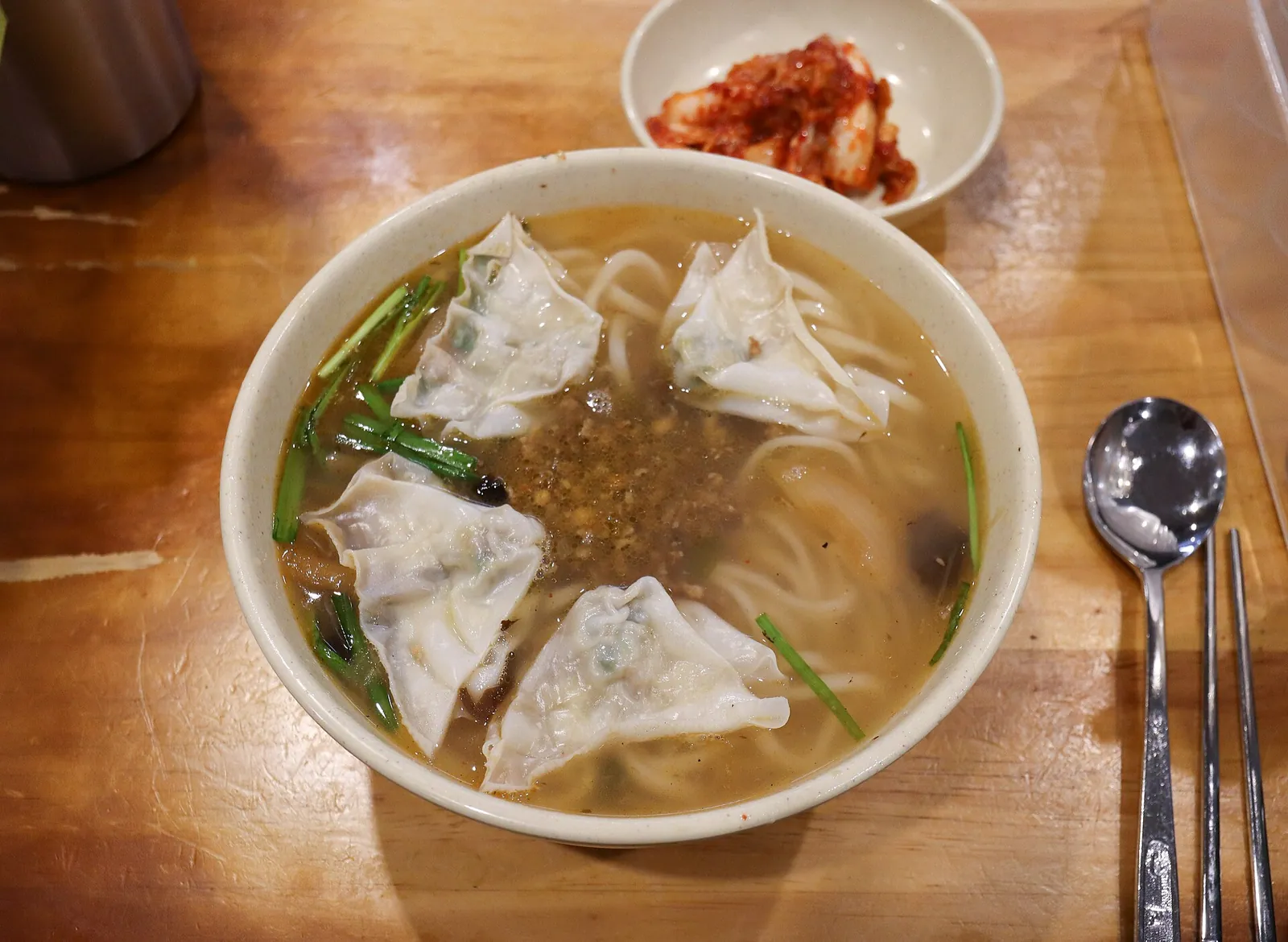 A bowl of kalguksu noodle soup with dumplings and a side dish of kimchi at Myeongdong Kyoja