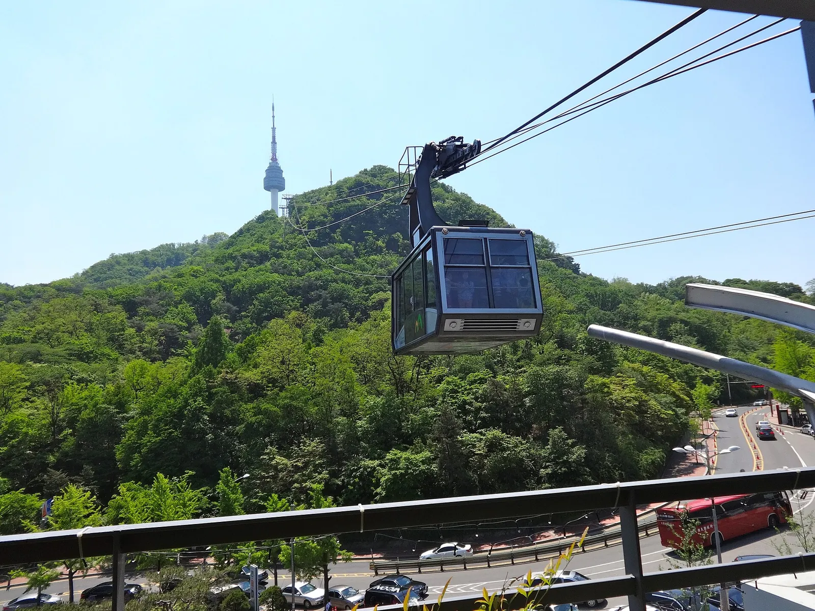 A Namsan Cable Car cabin on its cable above green slopes, with N Seoul Tower on the hilltop behind