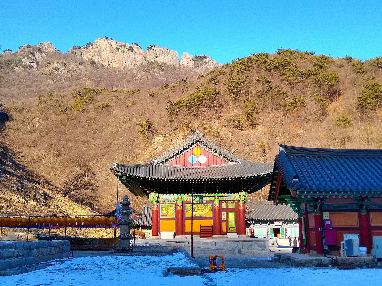 A brightly painted hall of Naejangsa temple under a rocky ridge of Naejangsan and a clear blue sky