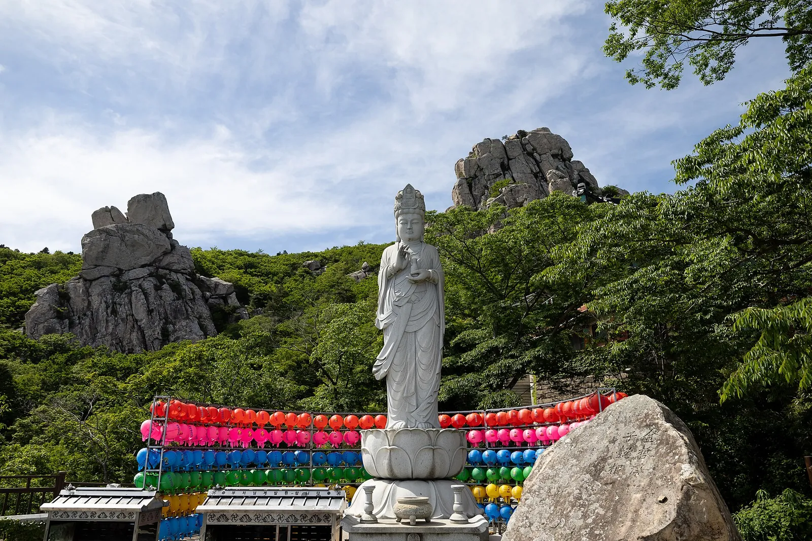 White stone Buddhist statue with rows of colourful lanterns below granite peaks at Boriam on Geumsan, Namhae