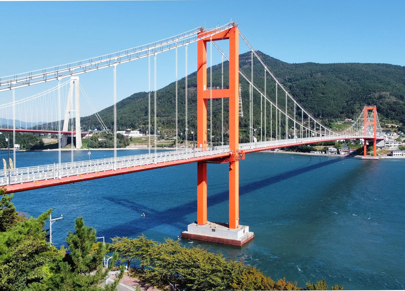 Red Namhae Bridge suspension bridge spanning a blue strait between wooded hills