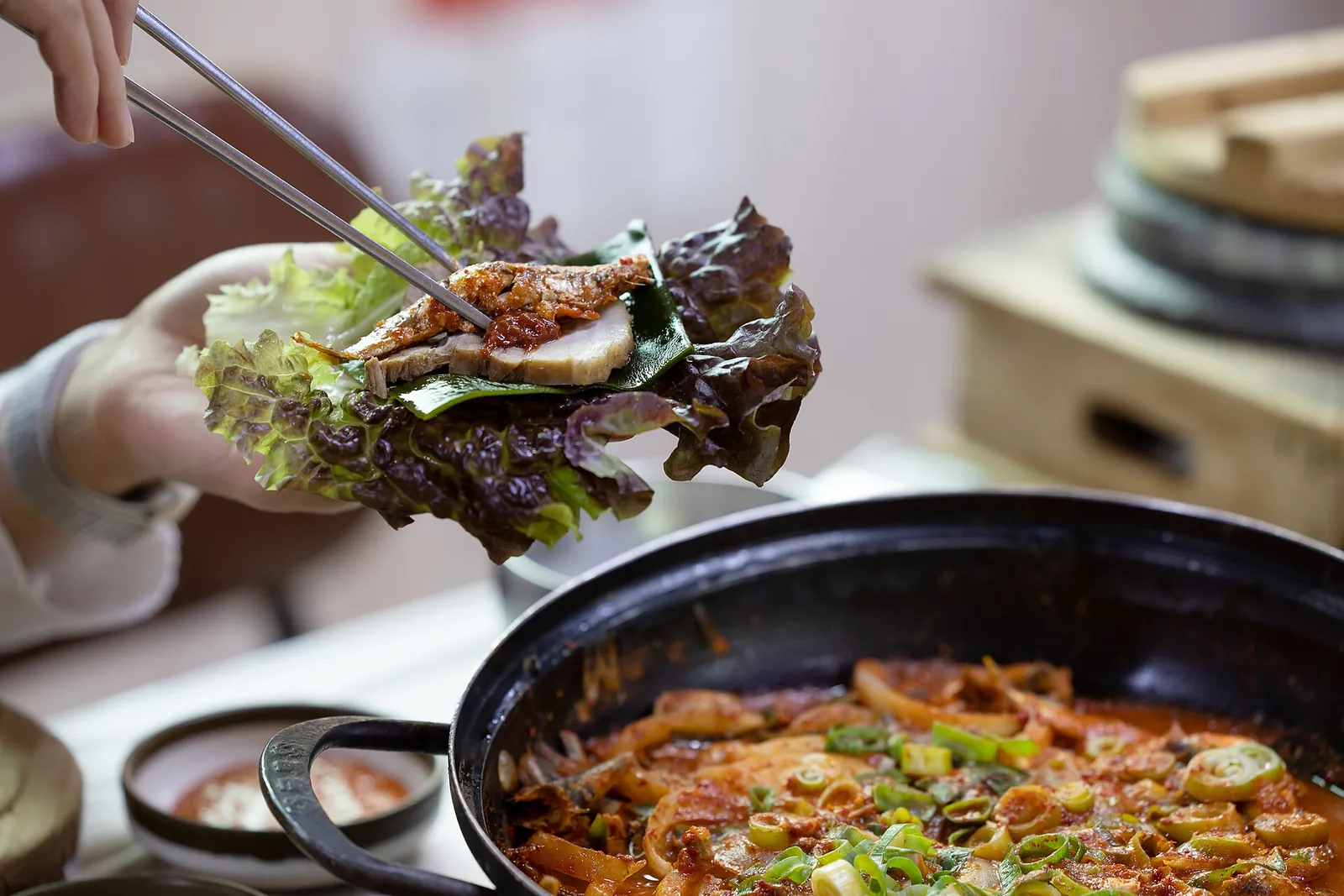A leaf wrap of rice and braised fish held with chopsticks above a pot of spicy braised fish in Namhae