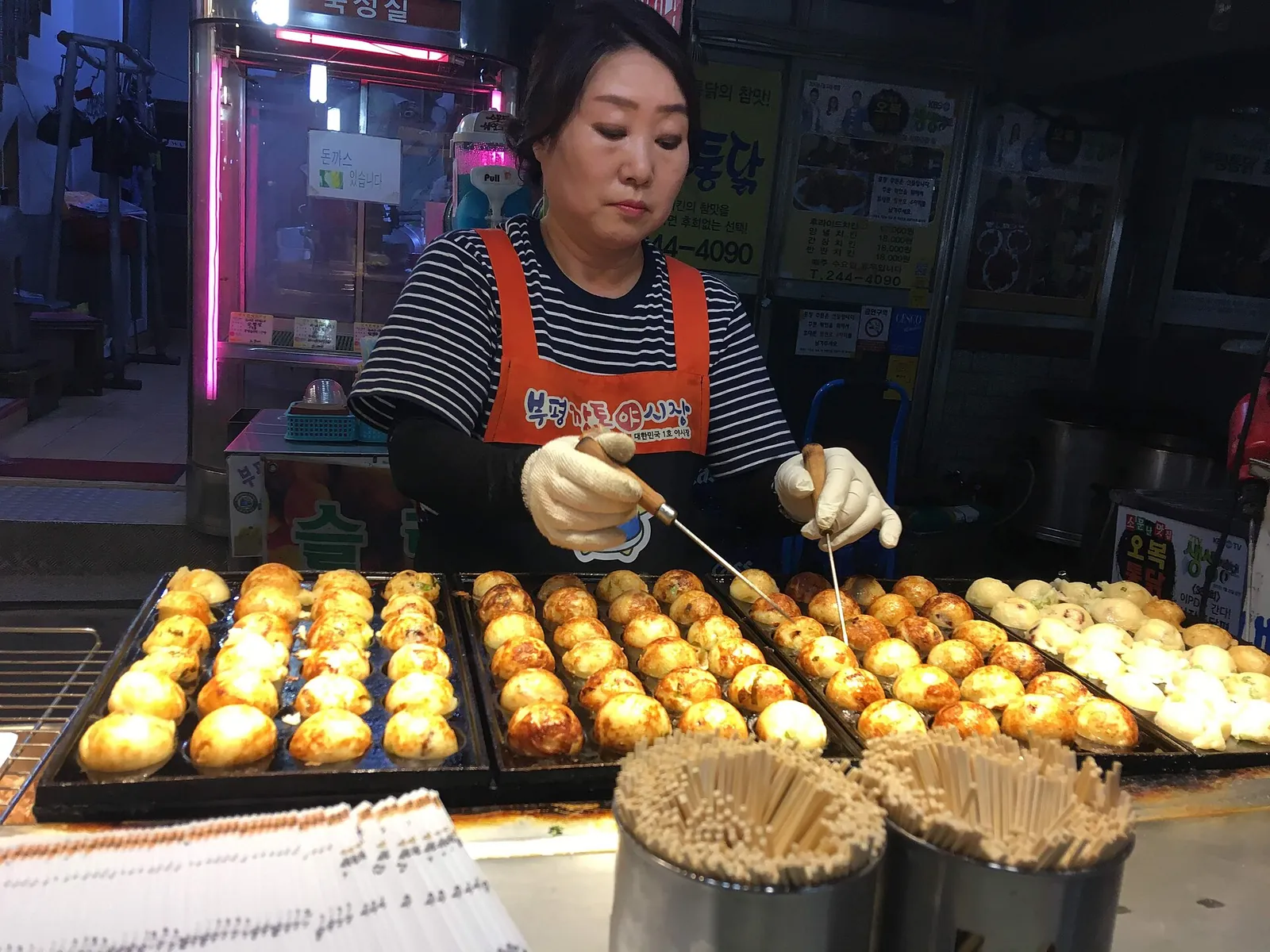 A vendor in an apron turning rows of round snacks on a griddle at Bupyeong Kkangtong Night Market