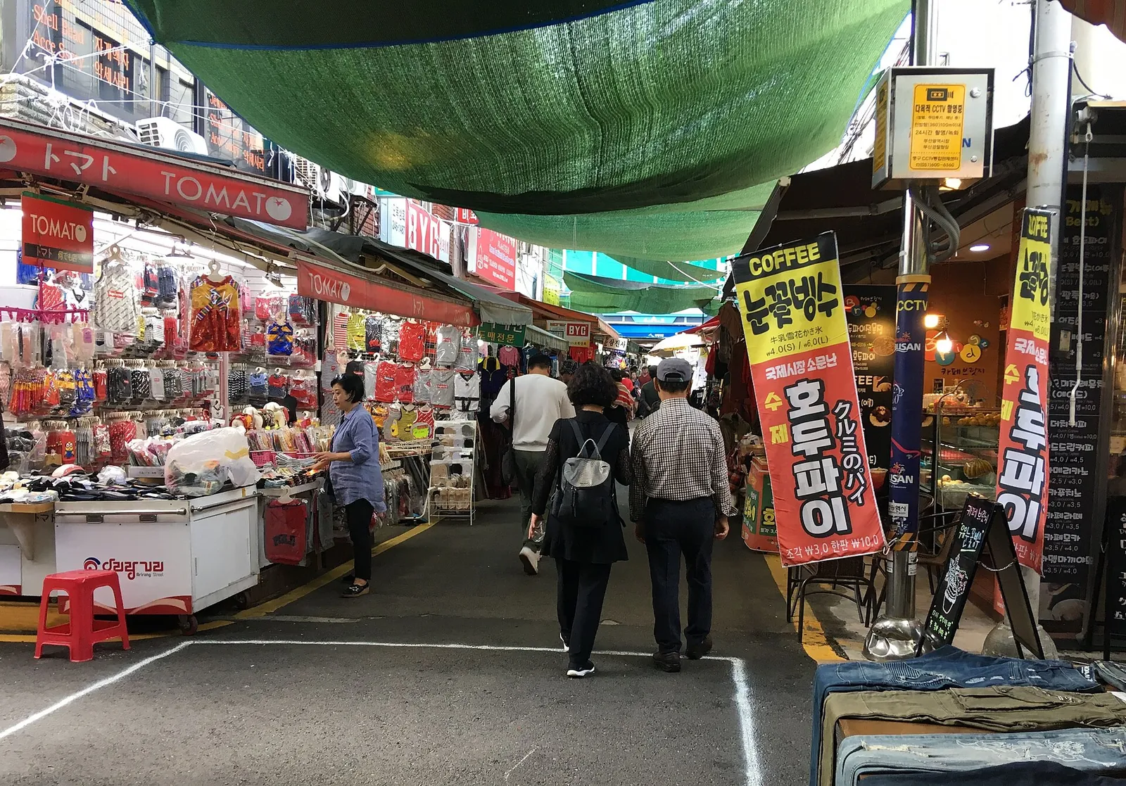 A covered lane in Gukje Market lined with clothing and goods stalls and walking shoppers