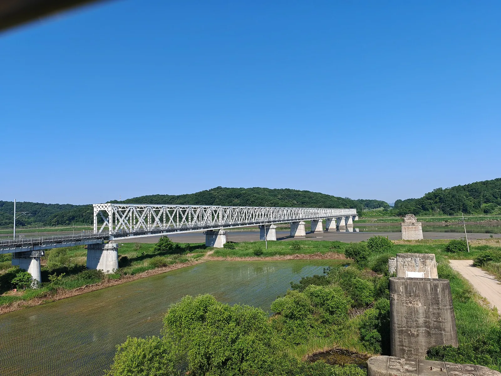 Steel truss railway bridge over the Imjingang River at Imjingak, with a concrete pier from an older bridge in the foreground