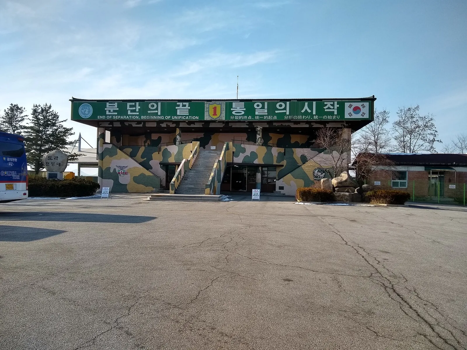 Camouflage-painted Dora Observatory building with a long green Korean signboard and a car park in front