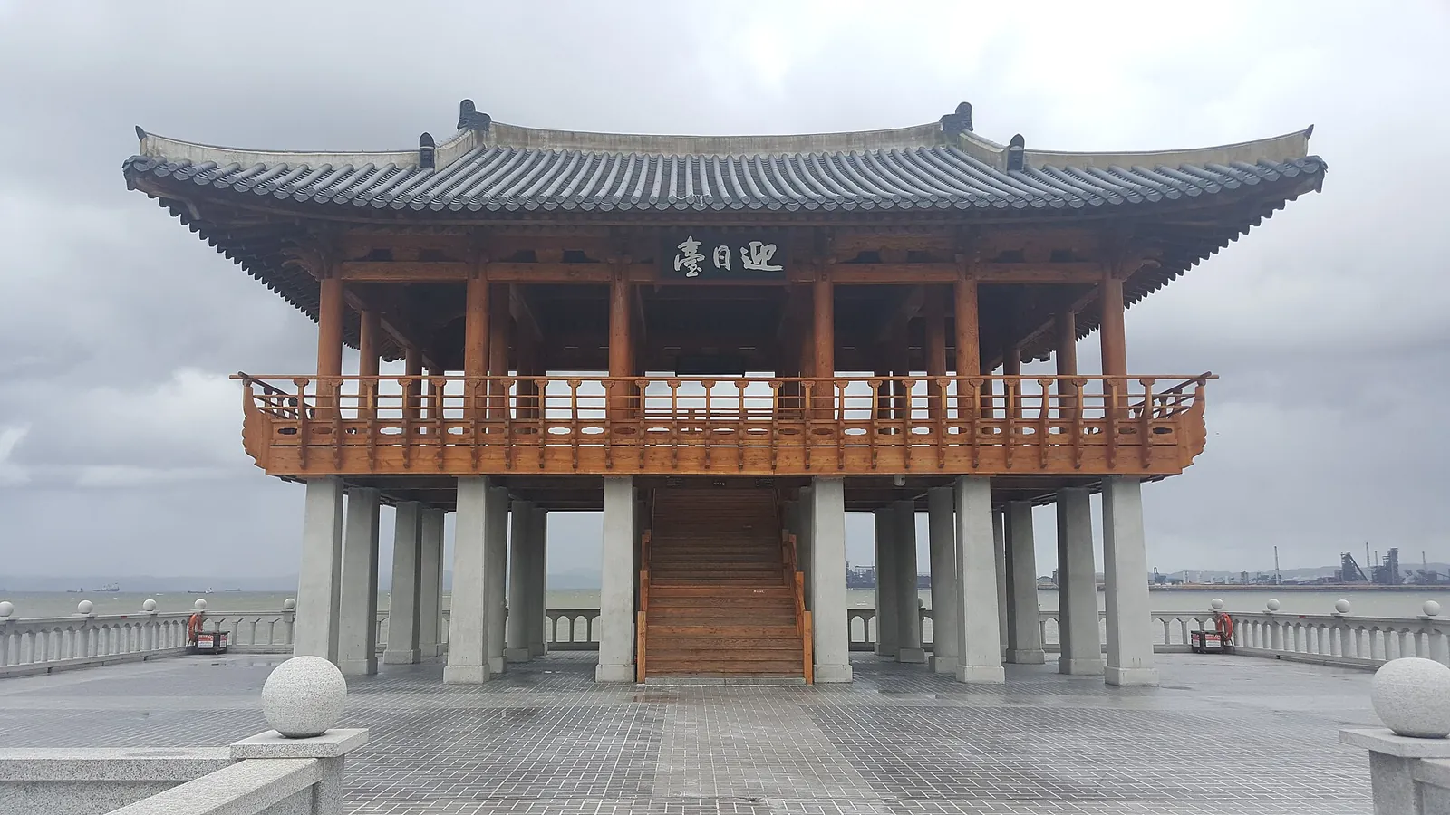 The two-storey wooden Yeongildae pavilion with a curved tiled roof standing over the sea under a grey sky