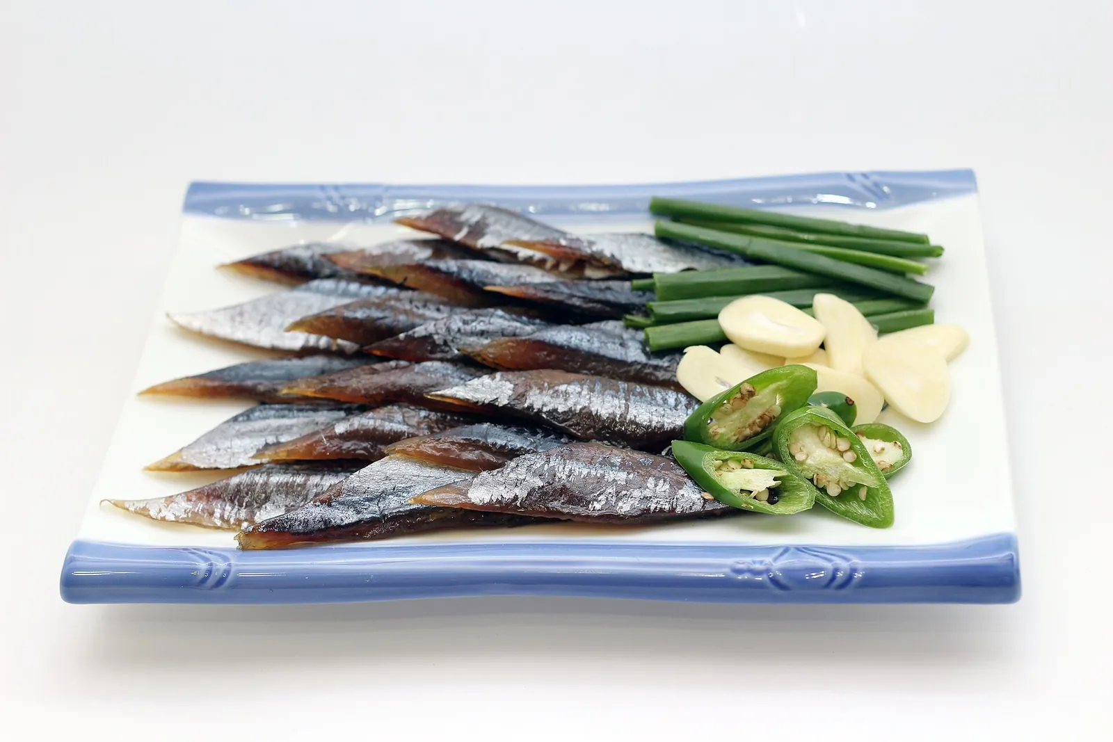 Strips of half-dried saury laid on a blue-rimmed plate with green onion, garlic and sliced green chilli
