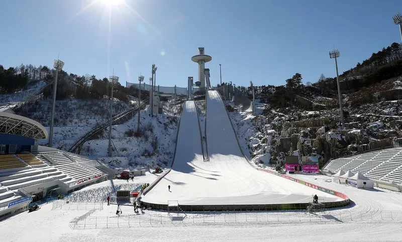 Snow-covered landing slope and tower of the Alpensia ski jumping stadium under a clear blue sky