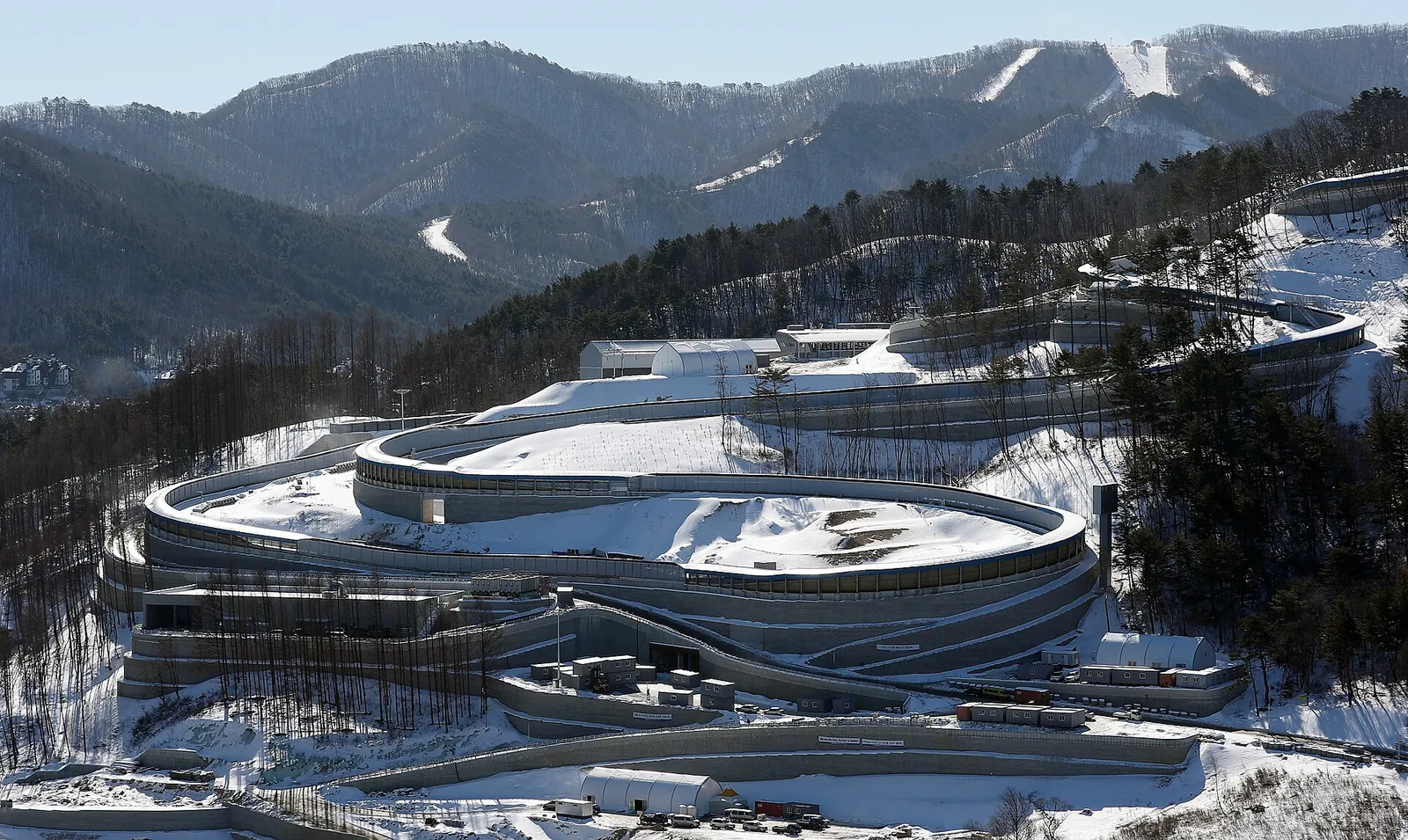 Curving concrete track of the Alpensia Sliding Centre in a snowy valley with ski slopes behind