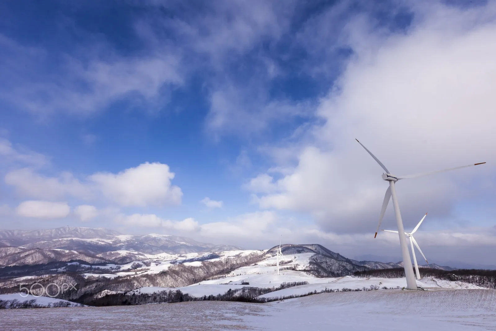 Wind turbine on a snowy ridge at Samyang Ranch under blue sky and white clouds