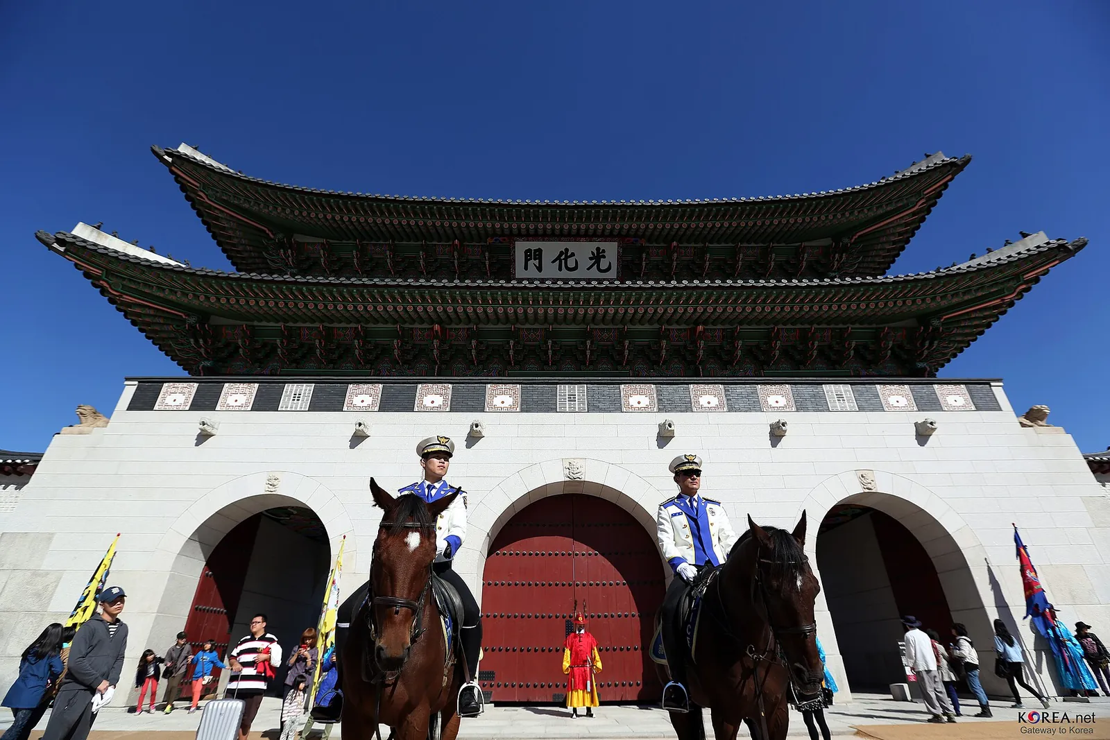 Mounted Korea Tourist Police officers in blue uniforms in front of Gwanghwamun Gate, Seoul, under a clear blue sky