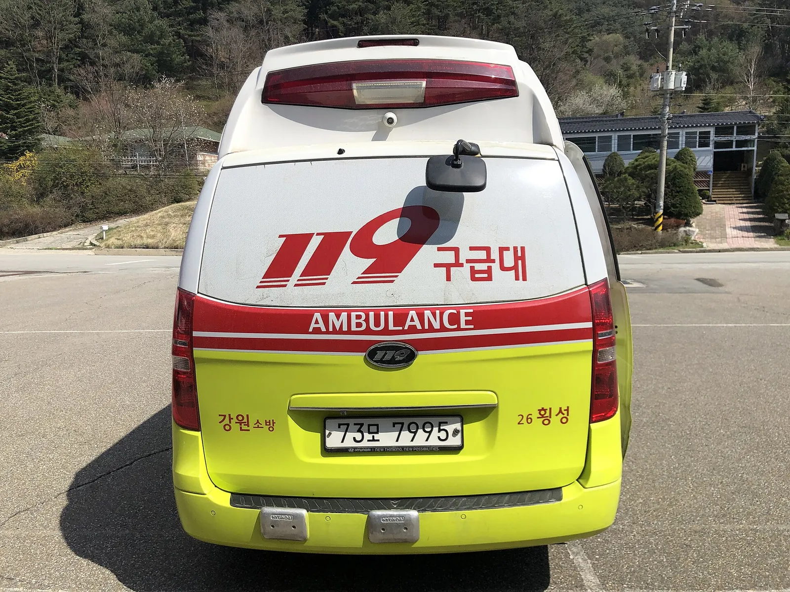 Rear view of a yellow-green and white 119 ambulance with Korean and English markings in a car park
