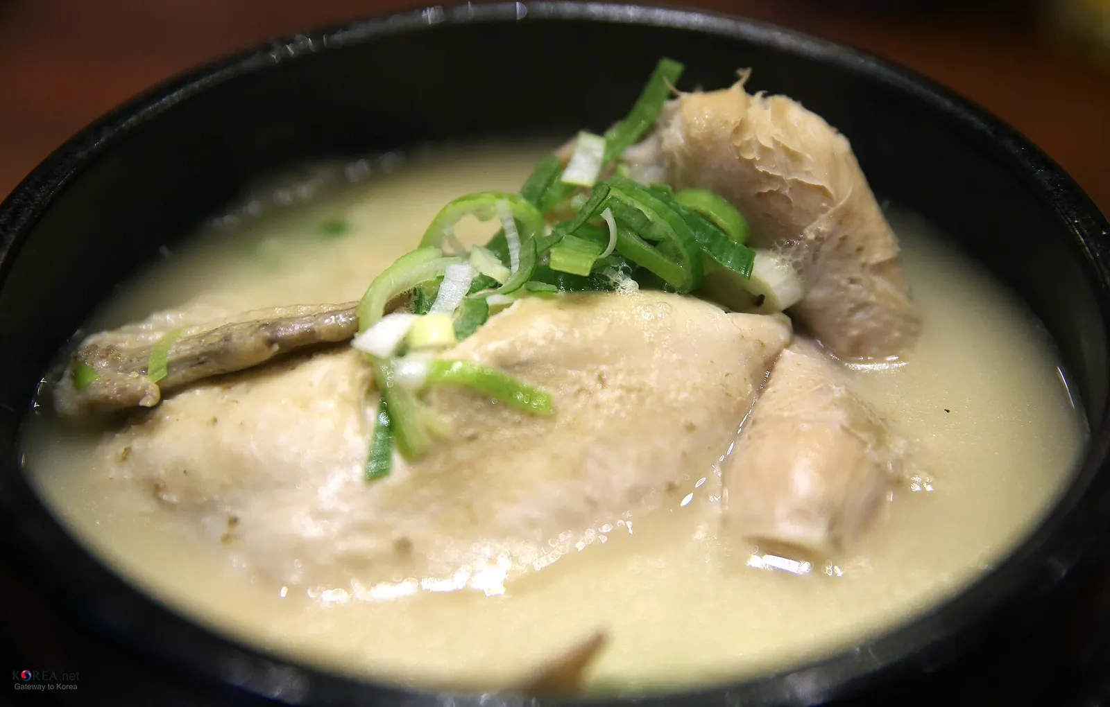 Bowl of samgyetang with a whole young chicken in milky broth topped with sliced green onion