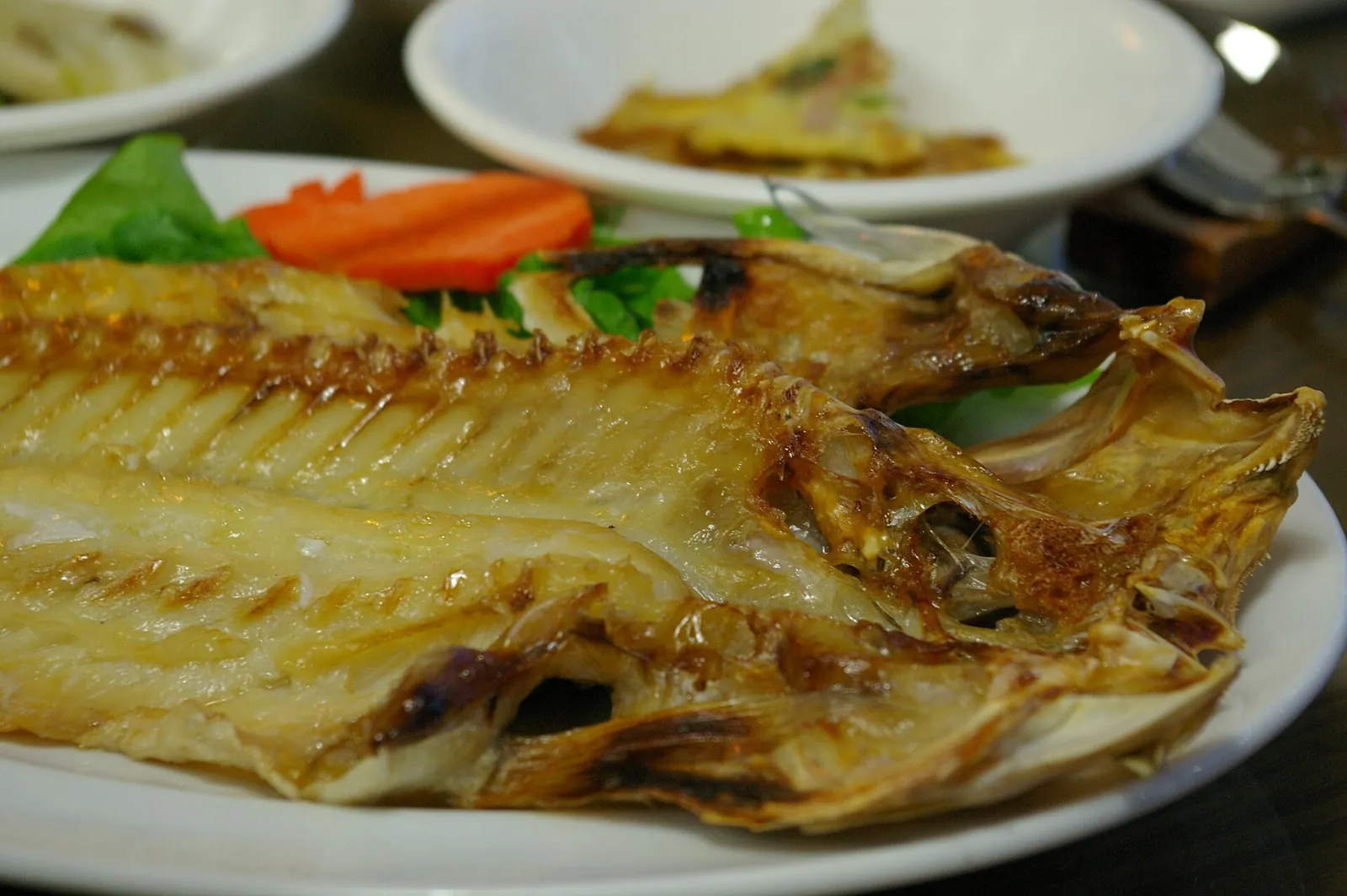 A whole grilled red tilefish on a white plate with side dishes