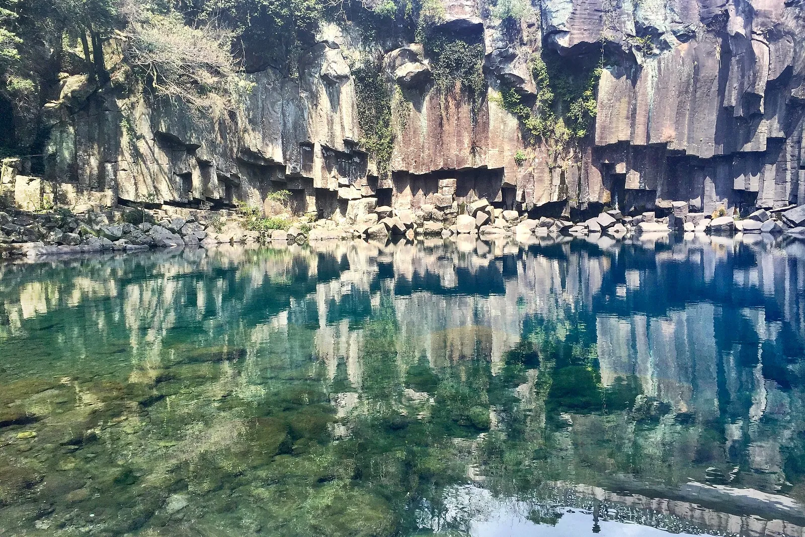 Turquoise pond reflecting a wall of grey basalt columns at Cheonjeyeon