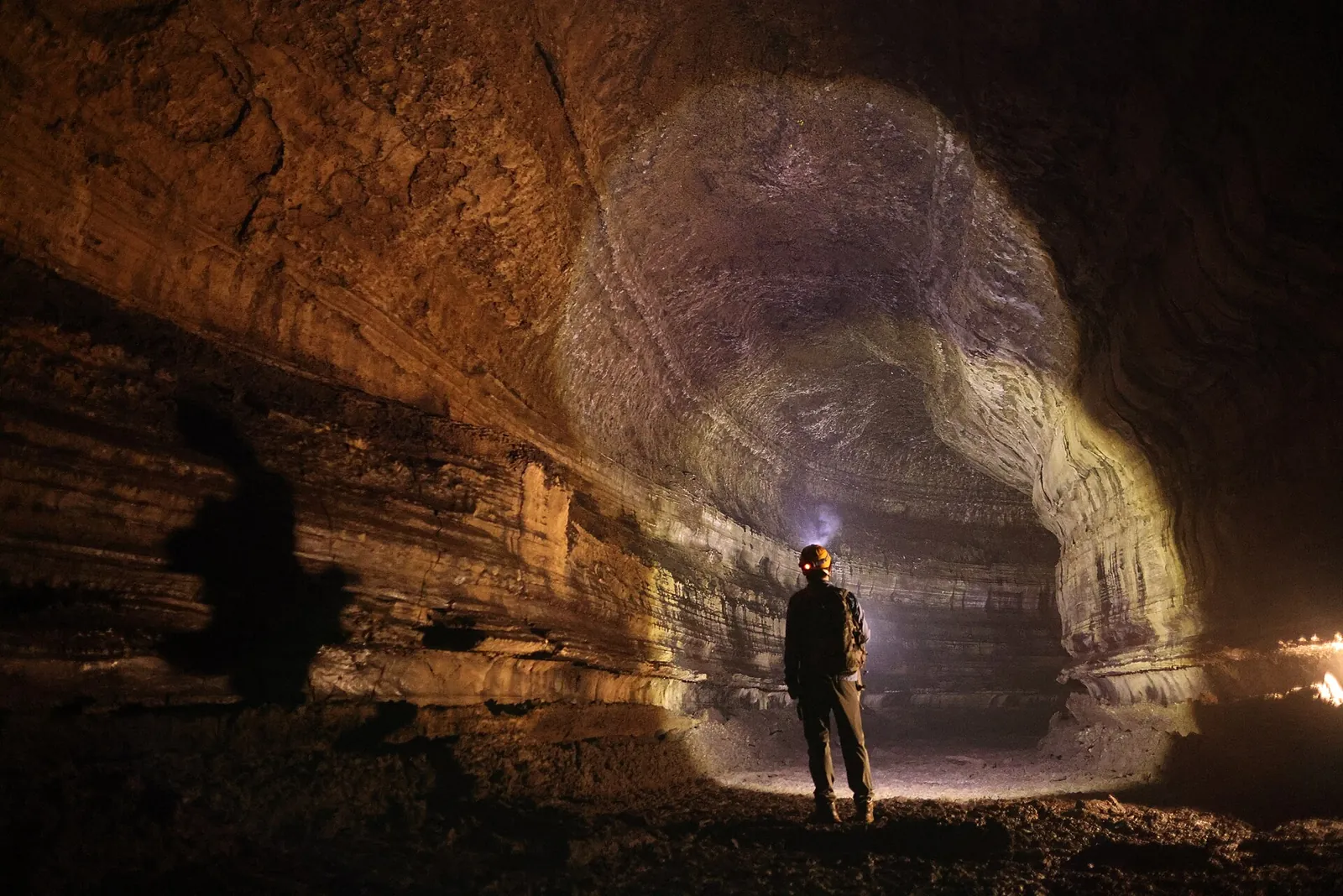 A visitor with a headlamp standing in the large, lit passage of Manjanggul lava tube