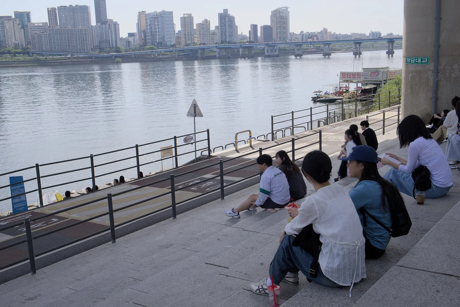 People sitting on the riverside steps of Ttukseom Hangang Park with the Han River and apartment towers beyond