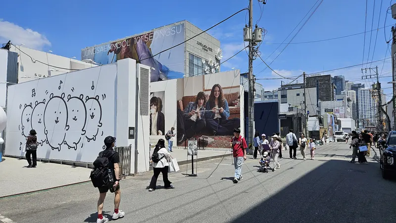 Pedestrians on a sunny Seongsu-dong street lined with a large mural wall and brand billboards