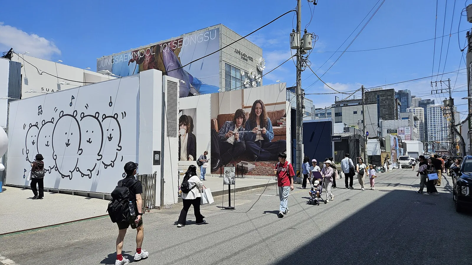 Pedestrians on a sunny Seongsu-dong street lined with a large mural wall and brand billboards