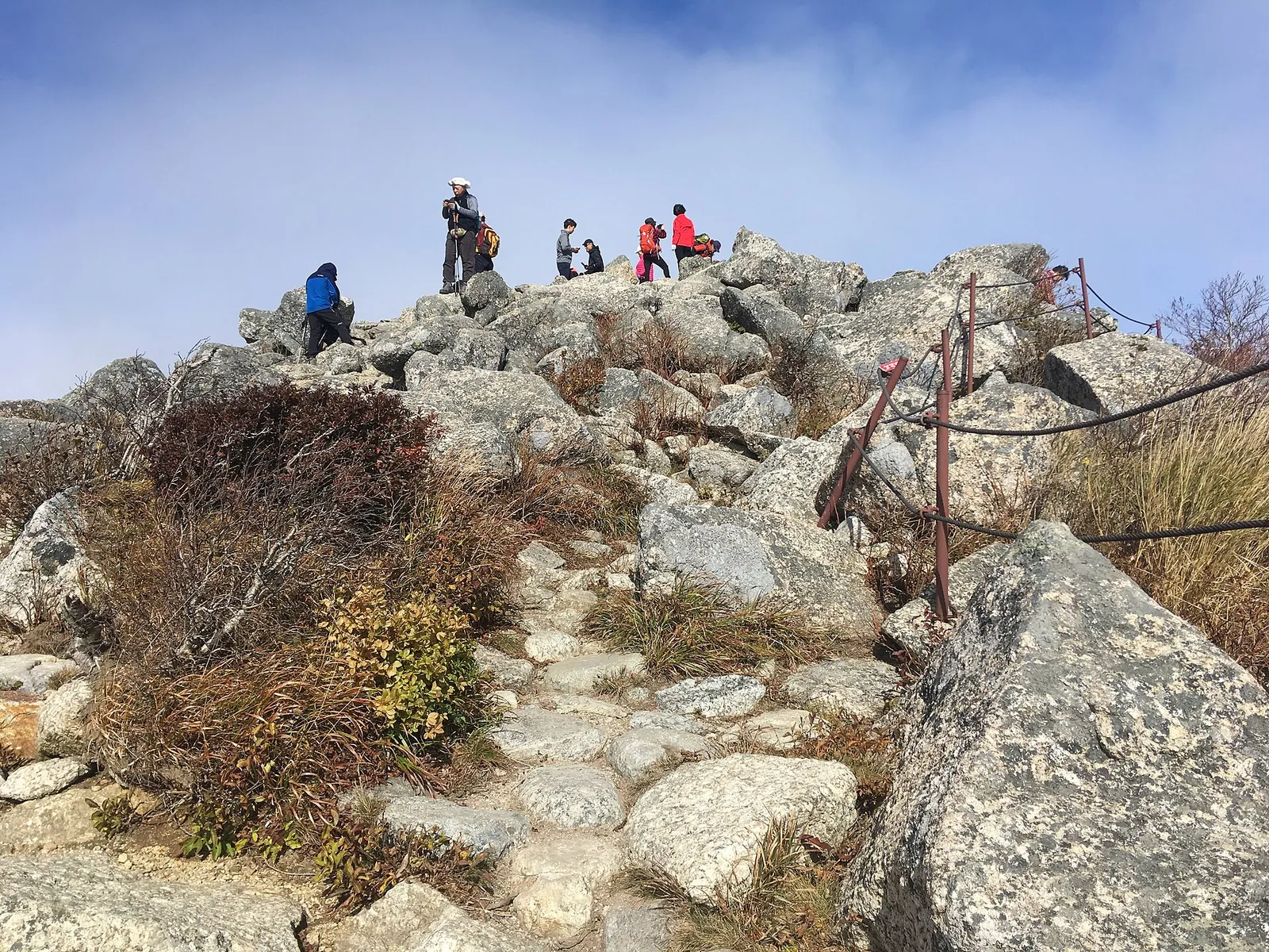 Hikers on the rocky summit of Daecheongbong with a rope-lined path in the foreground