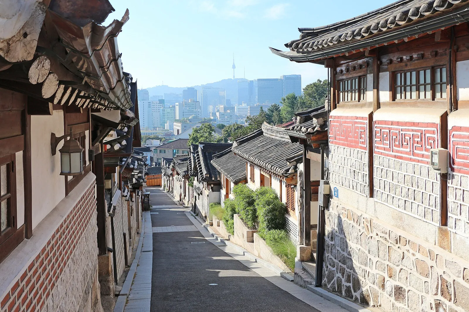 A lane of tiled hanok houses in Bukchon Hanok Village with Namsan Seoul Tower and the city skyline in the distance