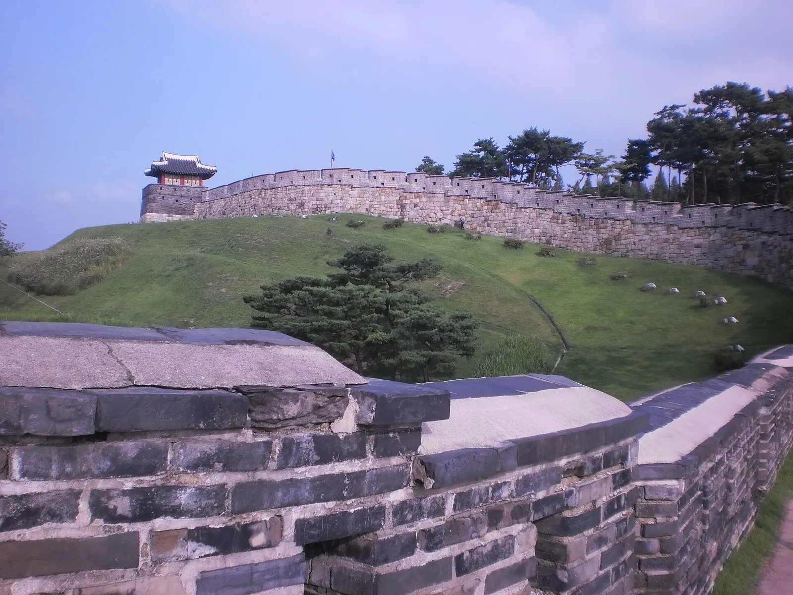 Stone wall of Hwaseong Fortress in Suwon curving over a grassy slope towards a watchtower