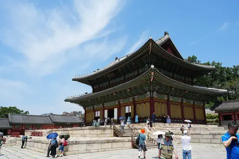 O Injeongjeon, o salão principal do Changdeokgung, visto do seu pátio de pedra sob um céu azul, com visitantes à frente