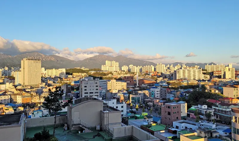 Rooftops of Sokcho with apartment towers and the Seoraksan ridges behind under a blue sky