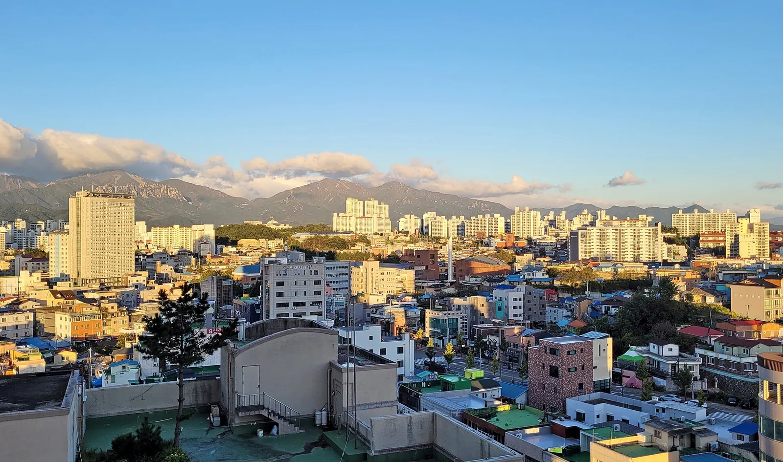 Rooftops of Sokcho with apartment towers and the Seoraksan ridges behind under a blue sky