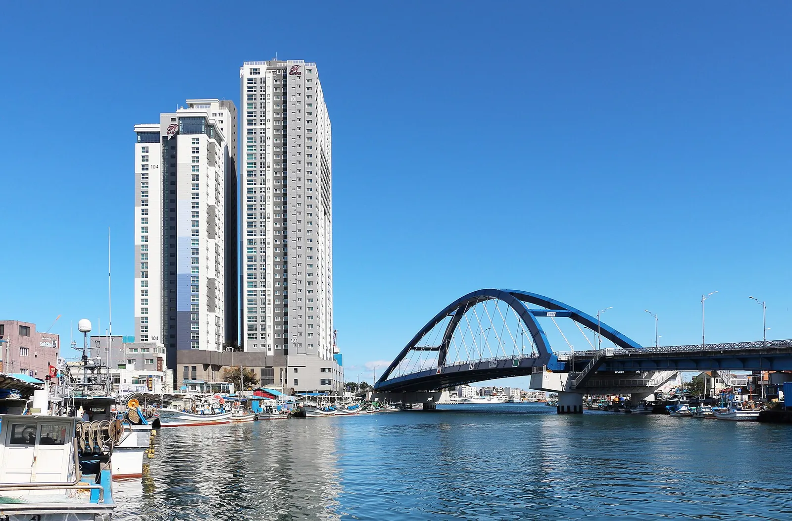 Arched Seorak Geumgang Bridge over Sokcho harbour with fishing boats and tall apartment towers