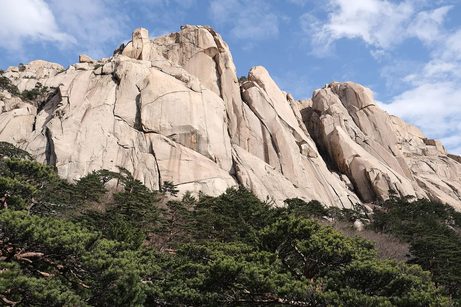A crista de granito pálido de Ulsanbawi a erguer-se acima de pinheiros sob um céu azul, no Parque Nacional de Seoraksan